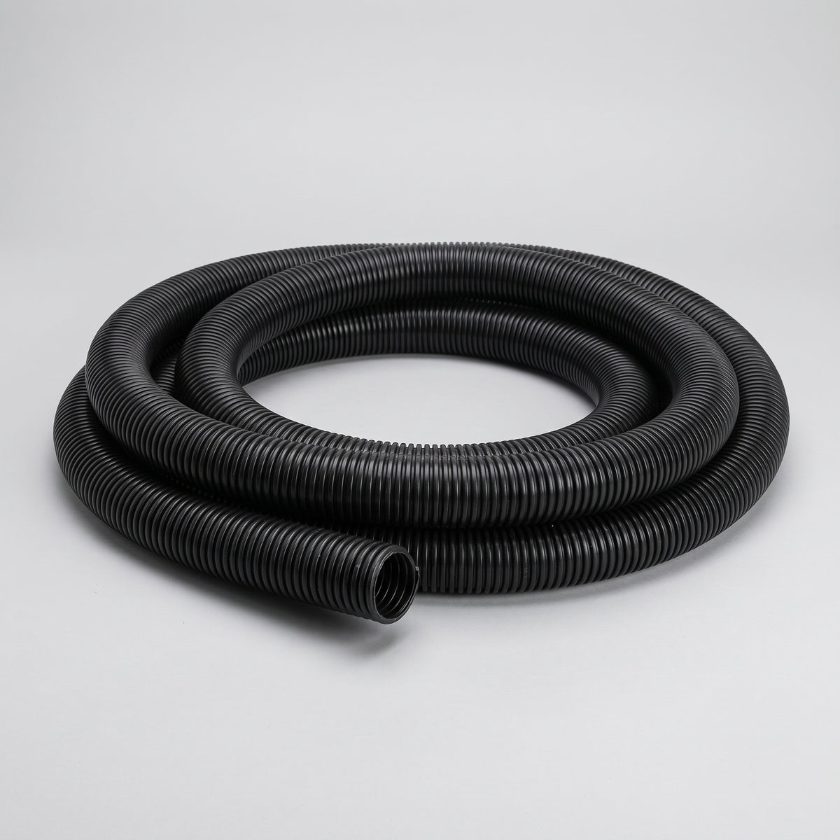 Coil of black spiral corrugated flexible pond hose on a plain grey background
