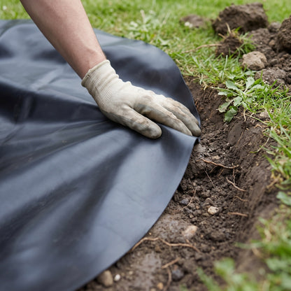 Gloved hand pressing black butyl rubber pond liner into the curve of a pond shelf