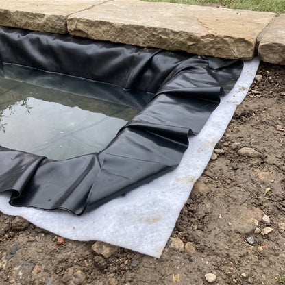 Black LDPE pond liner pleated into a pond corner over underlay, edge under stone coping