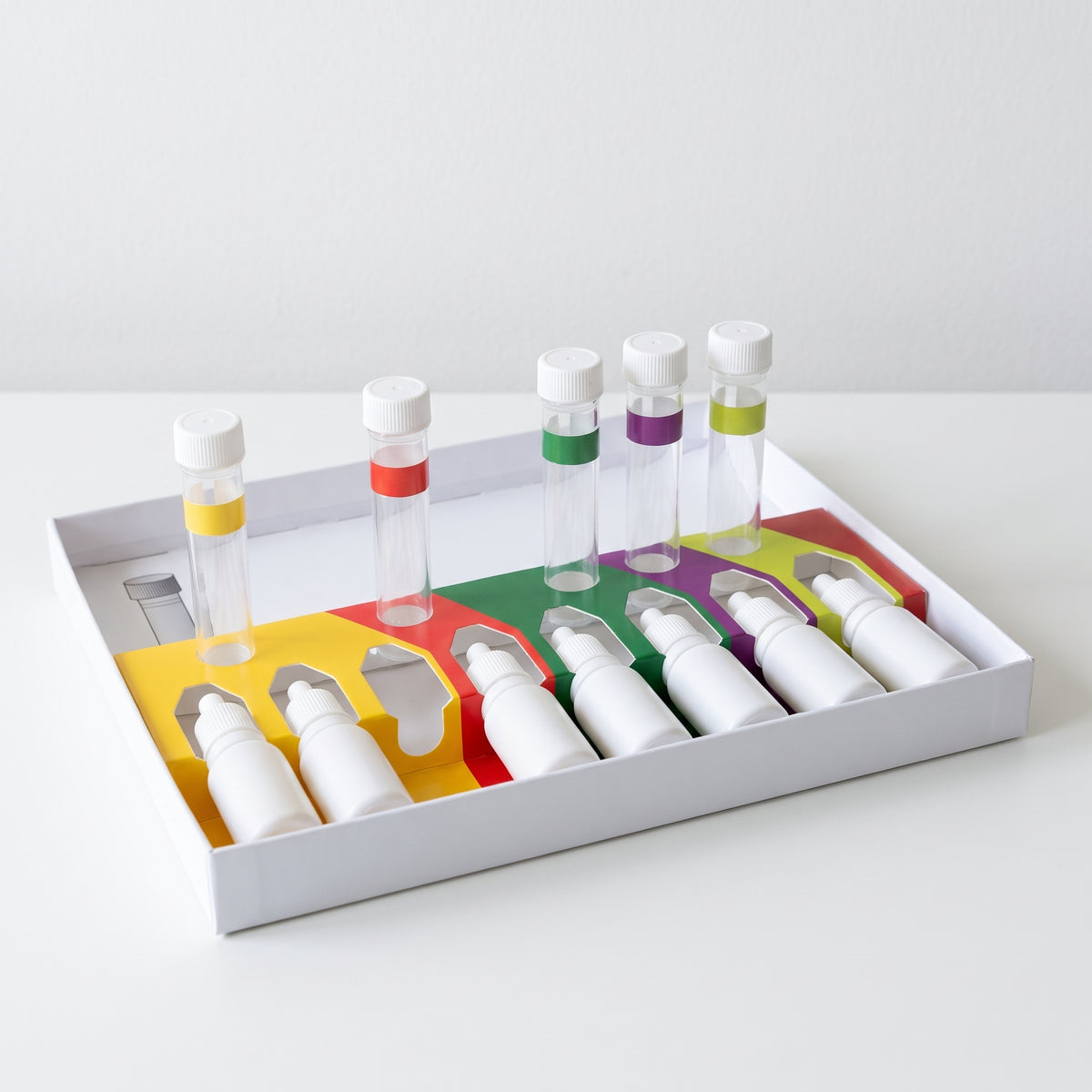 Liquid pond water test kit tray with colour-coded sections, white dropper bottles and capped test tubes on a white table
