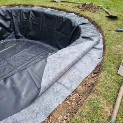 Close-up of black LDPE pond liner laid on top of grey geotextile underlay at the edge of a new pond