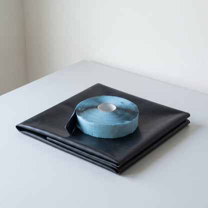 Pond liner repair kit: folded black liner patch with a roll of double-sided cold-glue tape on blue wax backing paper