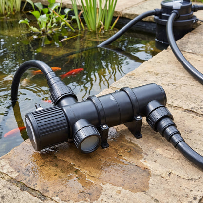 Inline pond UV clarifier connected between the pond pump and filter with black flexible hose, on the paving beside a clear garden pond