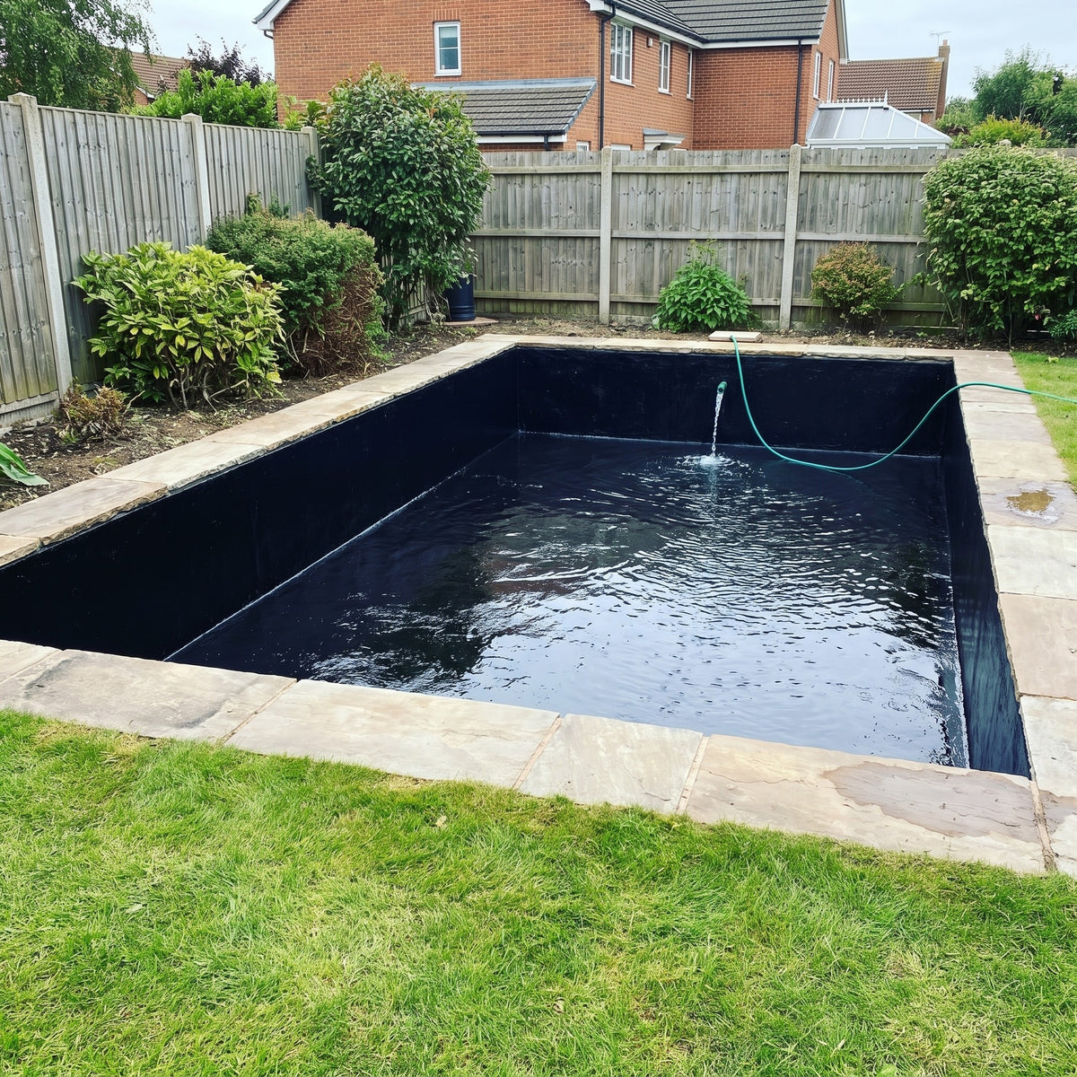 Rendered concrete garden pond sealed with PondLinersco Black Pond Sealer, glossy black finish, filling with water