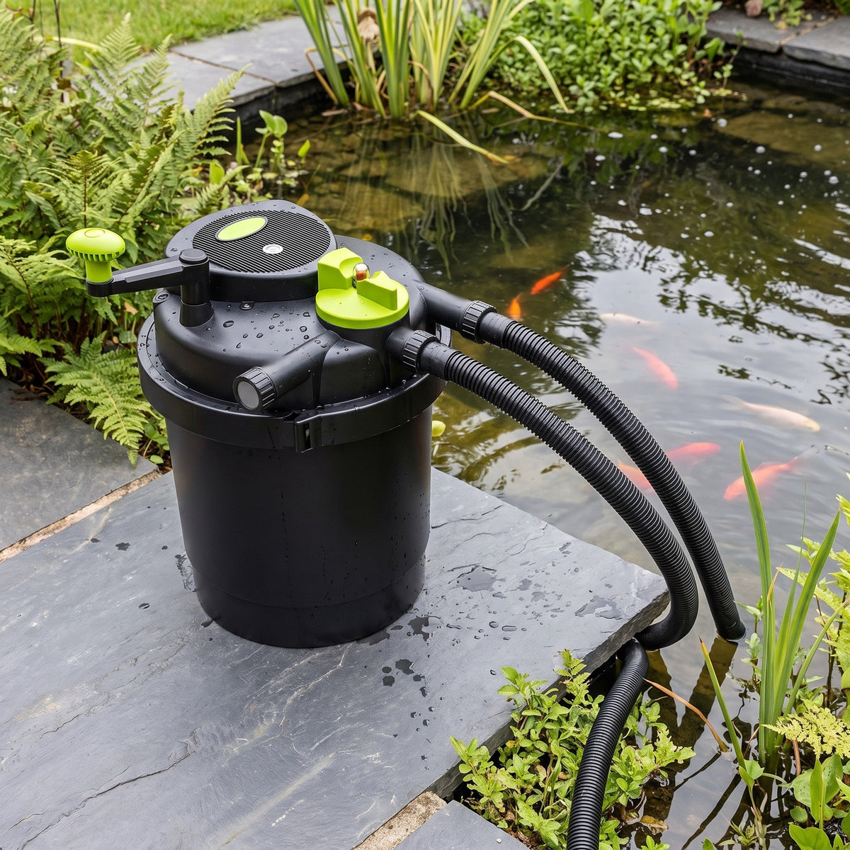 Pressurised UV pond filter with lime-green turn-to-clean handle standing on a slab beside a UK garden fish pond, hoses running into the water