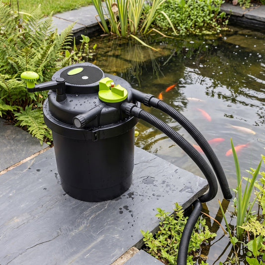 Pressurised UV pond filter with lime-green turn-to-clean handle standing on a slab beside a UK garden fish pond, hoses running into the water