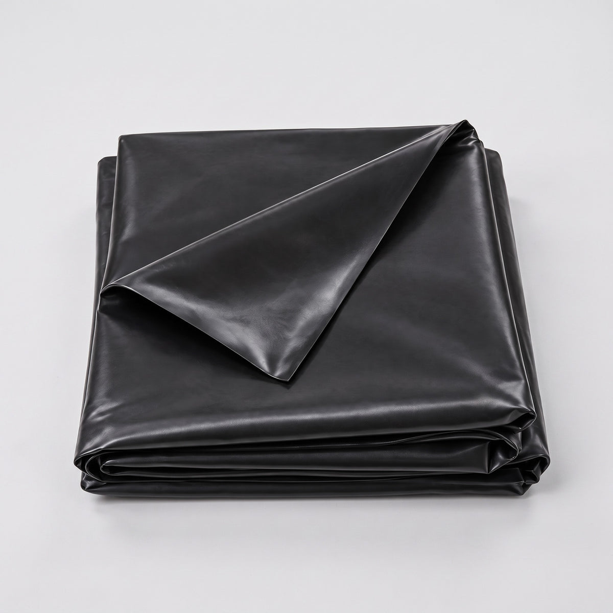 Folded black PVC pond liner with one corner turned back on a plain grey background