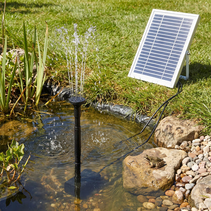 Small solar fountain pump kit in a wildlife pond with its framed solar panel on the bank beside a frog on a stone